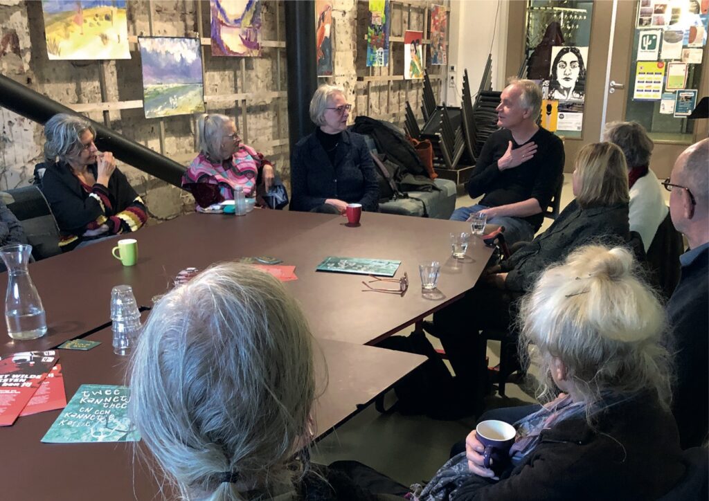 Buurtbewoners zitten met elkaar rond de tafel voor het cultureel cafe.